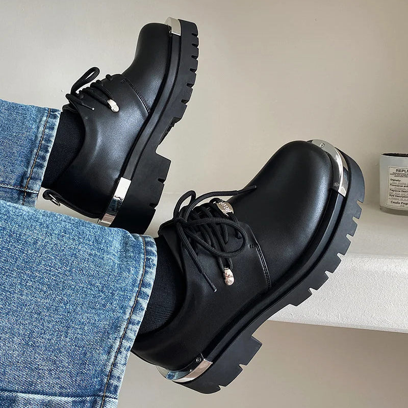 Black leather shoes with metal accents worn with blue jeans on a neutral background