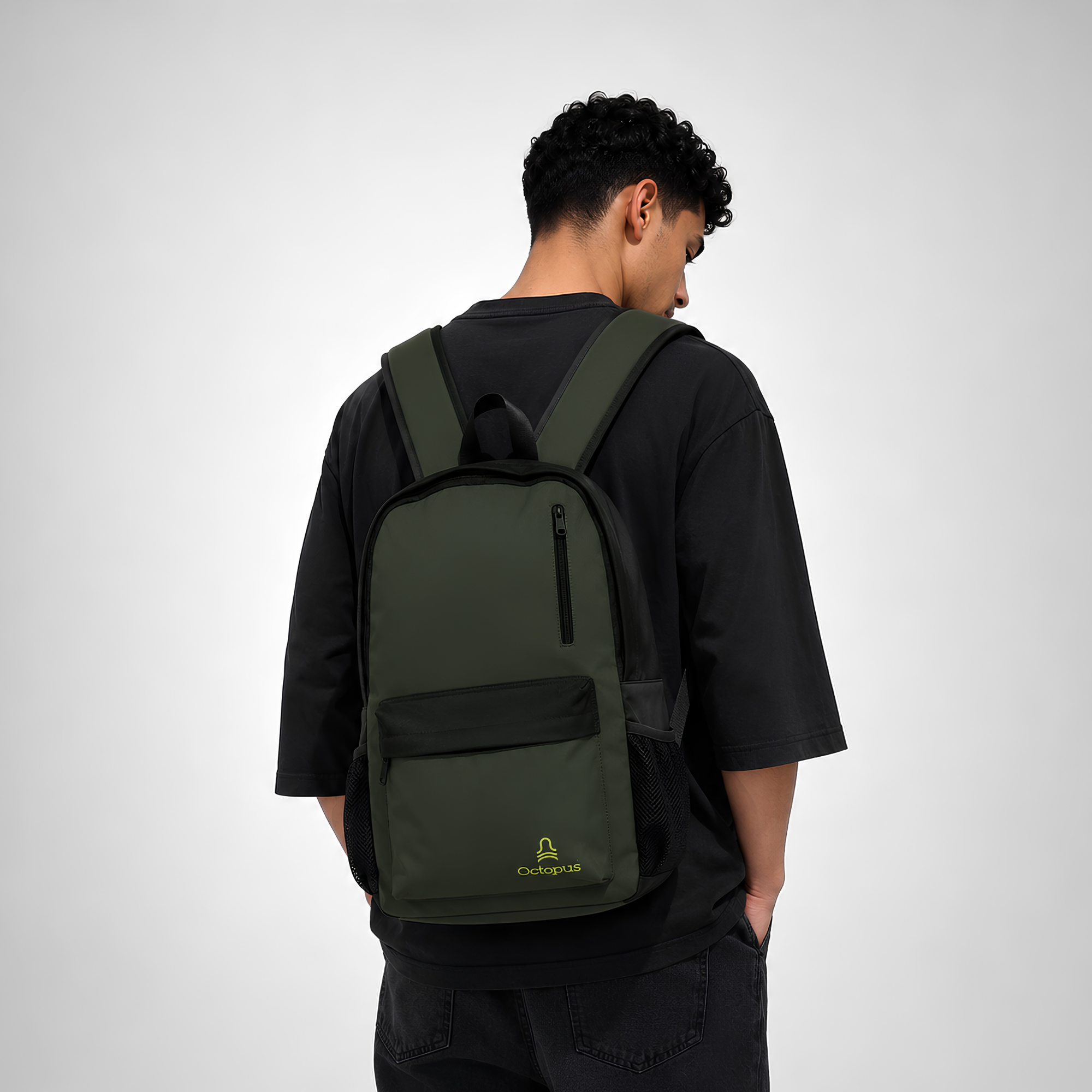 a young man wearing black clothes wearing a green laptop backpack with yellow octopus cairo on the front pocket