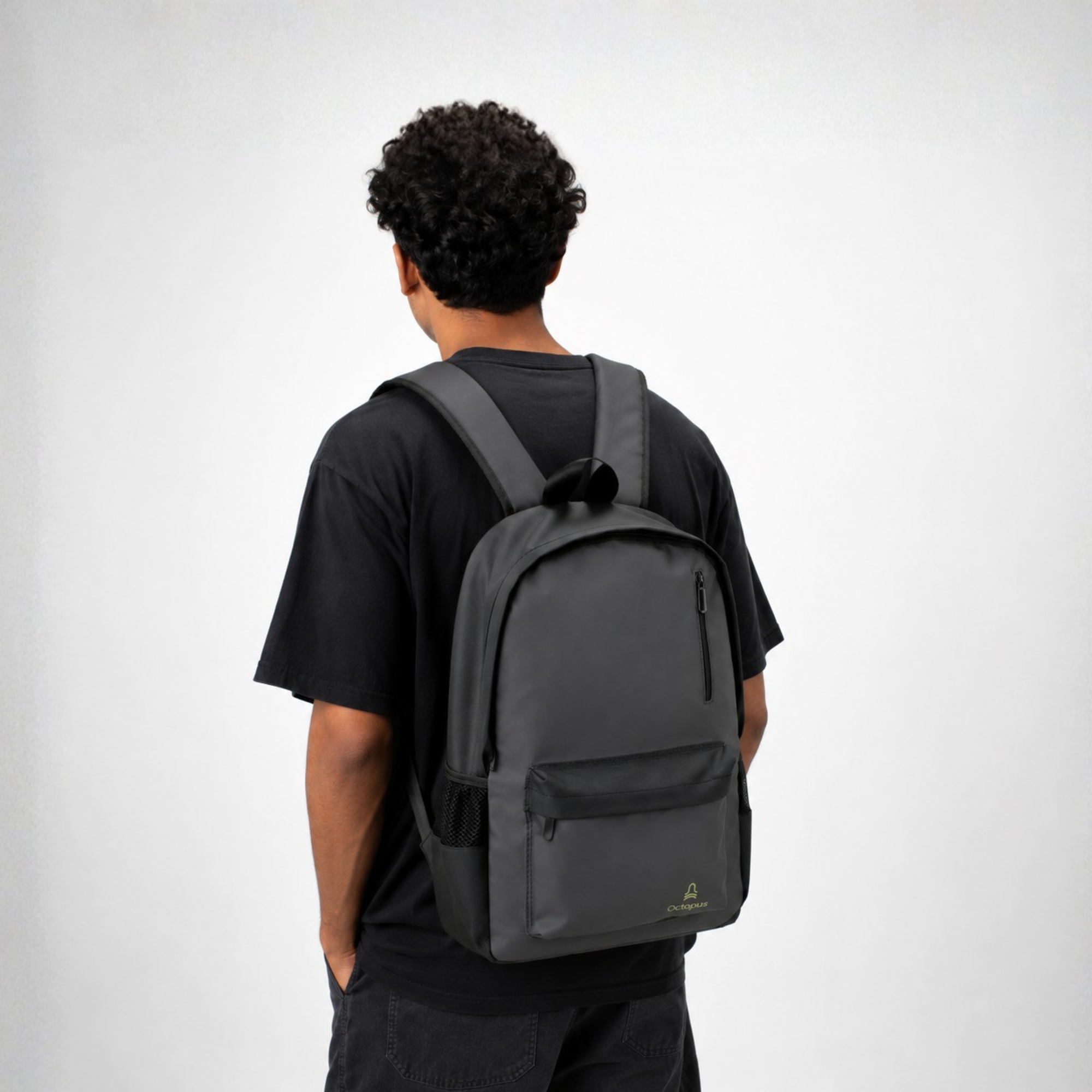 a young man in black clothes wearing a grey laptop backpack with black side pockets and a yellow octopus cairo logo on the front pocket.